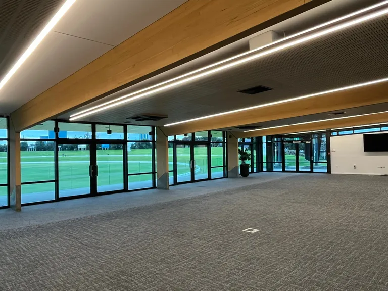 Function room in the Bay Oval pavilion: timber-lined ceiling and full-height glazing looking out over the cricket ground