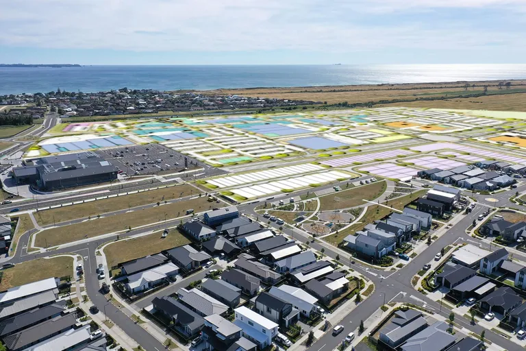 Aerial view of The Sands, Papamoa: completed housing in the foreground, colour-coded future stages and the town centre beyond, coast on the horizon