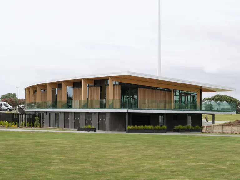 Completed two-storey pavilion with timber-clad upper level and a glazed balcony overlooking a playing field